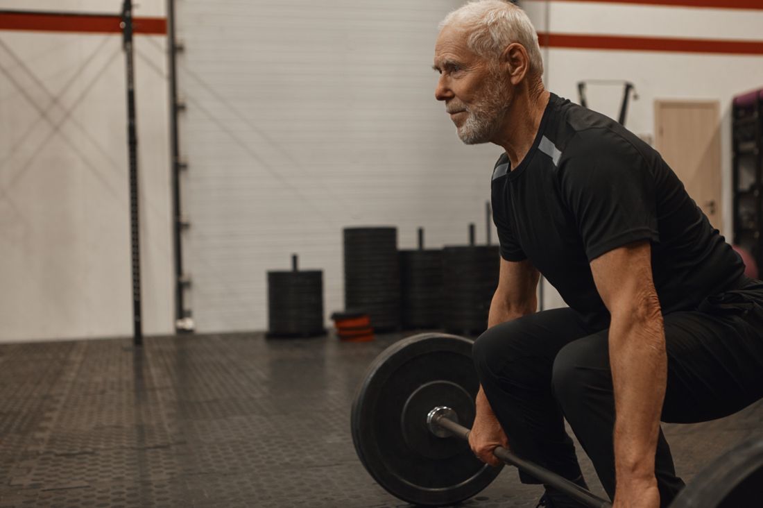 An older man lifting a barbell in the gym